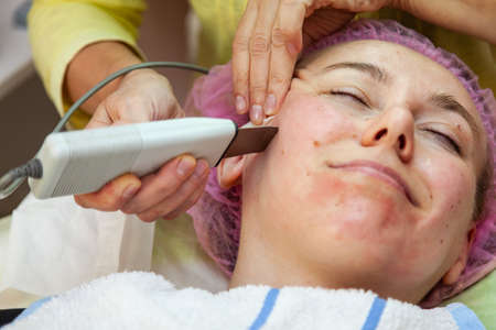 A young girl is lying on couch with a pink hat on her hair while performing an ultrasonic face...