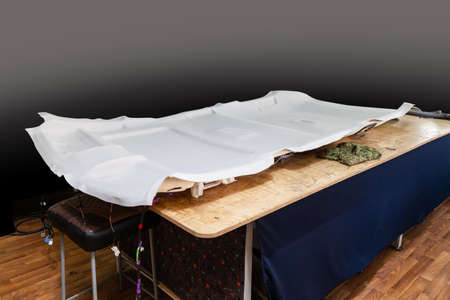 Gray ceiling lining removed from the car for tuning and bracing with grey soft material on a table...