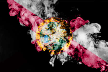 The national flag of the US state Florida in against a gray smoke on the day of independence in different colors of blue red and yellow. Political and religious disputes, customs and delivery.の写真素材