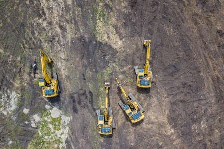 Aerial view of the four yellow crawler excavators that stand on the ground near the construction site and await the start of the working day digging the ground during the buildings and roads.の写真素材