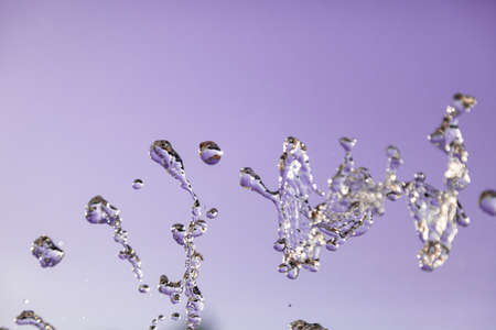 Water droplets frozen in the air with splashes and chain bubbles on a pink and purple isolated...