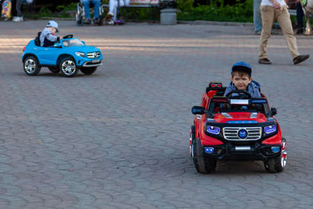 Novosibirsk, Russia - 05.28.2019: Two little boys ride on red and blue electric cars while walking...