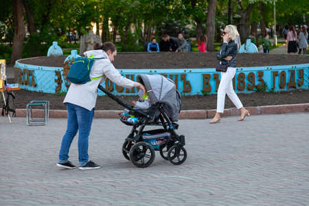 Novosibirsk, Russia - 05.28.2019: Young mom girls with strollers and small children are walking in a city park against a background of green treesのeditorial素材