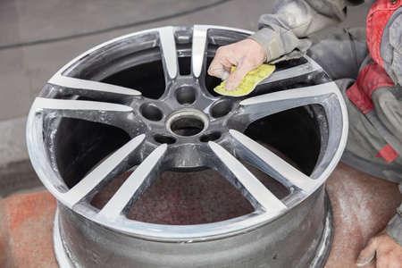 Master body repair man is working on preparing the surface of the aluminum wheel of the car for subsequent painting in the workshop, cleaning and leveling the disk with the help of abrasive materialの写真素材