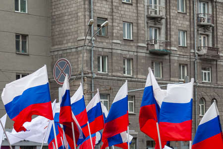 A large number of Russian flags in tricolor with stripes of white, blue and red against the background of the walls of buildings with gray windows during a rally or paradeの写真素材