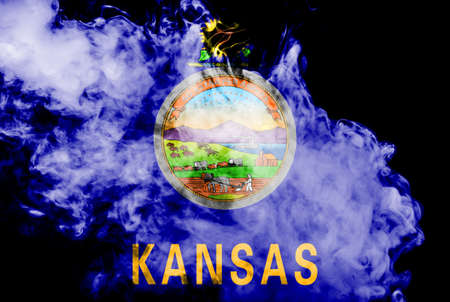 The national flag of the US state Kansas in against a gray smoke on the day of independence in different colors of blue red and yellow. Political and religious disputes, customs and delivery.の写真素材
