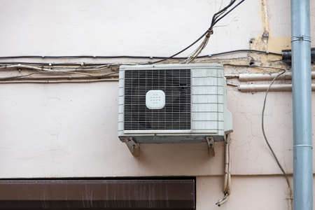 White air conditioning on the old wall of the house with the old wires of communication on the plastic drain pipe above the window. Cooling and comfort at home in the hot season.の写真素材