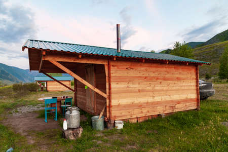 A simple wooden house for temporary living in the summer in the Altai Mountains with a chimney on the roof in a picturesque place with green grass and trees. Travel and nature.の写真素材
