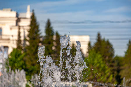 City fountain with splashes and jets of water against the background of buildings and green trees...