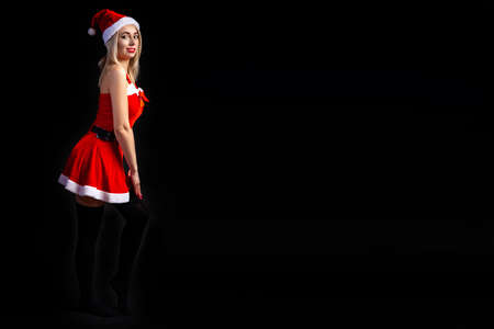 Young beautiful blonde girl in a sexy red Snow Maiden costume or Santa Claus on a black isolated background in the Christmas and New Year 2020 holidays with the place for textの写真素材