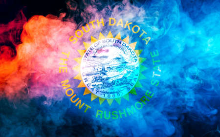 The national flag of the US state South Dakota in against a gray smoke on the day of independence in different colors of blue red and yellow. Political and religious disputes, customs and delivery.の写真素材