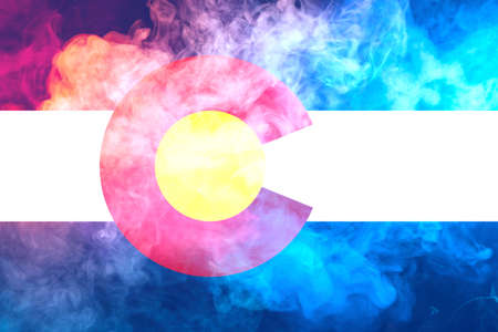 The national flag of the US state Colorado in against a gray smoke on the day of independence in different colors of blue red and yellow. Political and religious disputes, customs and delivery.の写真素材