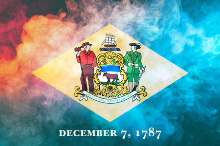 The national flag of the US state Delaware in against a gray smoke on the day of independence in different colors of blue red and yellow. Political and religious disputes, customs and delivery.の写真素材