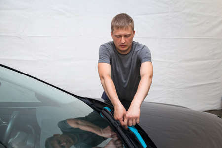 A man of Caucasian appearance with blue paper tape plasters a body element wipers with a black car...