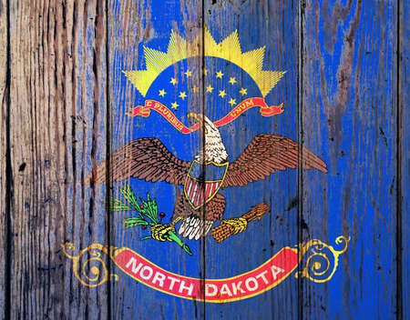 North Dakota US state national flag on a gray wooden boards background on the day of independence in different colors of blue red and yellow. Political and religious disputes, customs and delivery.の写真素材