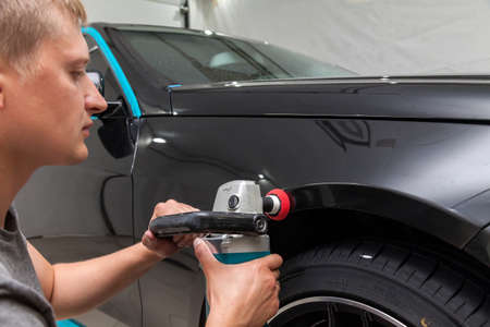 The polisher polishes the body of the vehicle with special wax to protect the car from minor scratches and damage, using a polishing machine to cover black fender after washing. Auto service industryの写真素材