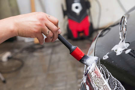 Novosibirsk, Russia - 07.19.2019: Close-up of a man's hand with a brush while cleaning the emblem of a Mercedes-Benz car on the hood of a black car while washing in the detaing workshop with foam soapのeditorial素材