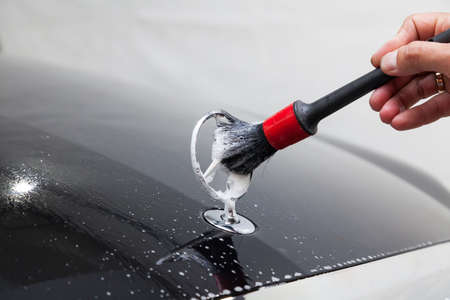 Novosibirsk, Russia - 07.19.2019: Close-up of a man's hand with a brush while cleaning the emblem of a Mercedes-Benz car on the hood of a black car while washing in the detaing workshop with foam soapのeditorial素材
