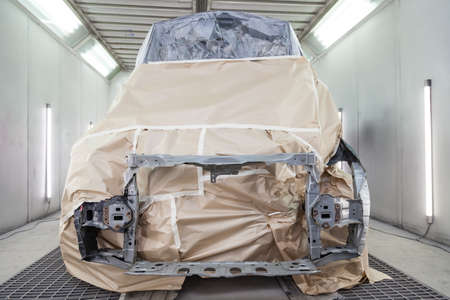 A black car is completely covered in paper and adhesive tape to protect against splash during painting and repair frame after an accident in a workshop for body repair of vehicles with bright lightingの写真素材