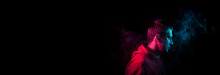 Banner with a portrait of a guy in profile face standing back to black background with a feeling of sadness and loneliness, around his head a cloud of blue and pink smoke. The soul and feelings of manの写真素材