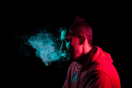 Close up portrait of the face of an adult serious man exhales green toxic smoke while smoking...