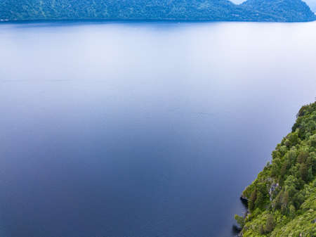 An aerial view of the Teletskoye Lake between the Altai Mountains on the shore on which there are green trees and other ships. Leisure and outdoor travel without people.の写真素材