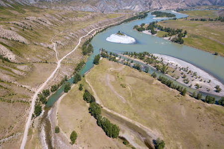 Landscape of the mountain chain of the Altai covered with green trees and rocks, with the turquoise Katun River and its rapids on a sunny summer day and a blue sky with white clouds. Tourist route.の写真素材