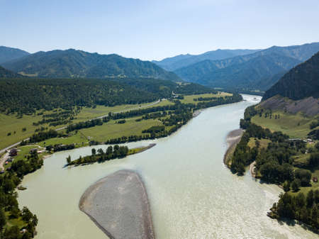Landscape of the mountain chain of the Altai covered with green trees and rocks, with the turquoise Katun River and its rapids on a sunny summer day and a blue sky with white clouds. Tourist route.の写真素材