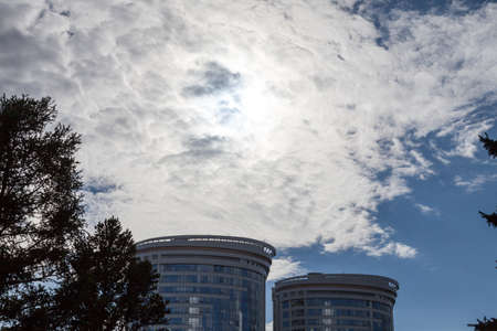 Top view on the upper floors and roofs of two identical skyscrapers with blue sky and white clouds in the background.の写真素材