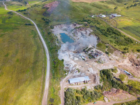 Aerial view of a small plant for the production and cleaning rubble and cement near the heaps of building materials from the pipe of which gray smoke goes, the tractor transports the finished product.の写真素材