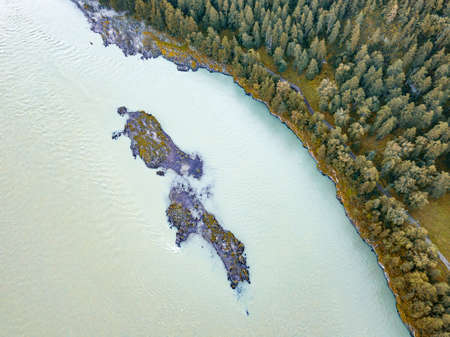 Aerial view of a small stone island on a green mountain river near the shore on which yellow trees grow on indian summerの写真素材