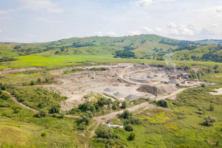 Aerial view of a small plant for the production and cleaning rubble and cement near the heaps of building materials from the pipe of which gray smoke goes, the tractor transports the finished product.の写真素材