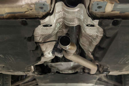 Close-up on the part of the bottom of the car from the front of the exhaust pipe and the catalyst disassembled during the repair in the workshop auto service vehiclesの写真素材