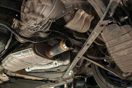 Close-up on the part of the bottom of the car from the front of the exhaust pipe and the catalyst disassembled during the repair in the workshop auto service vehiclesの写真素材