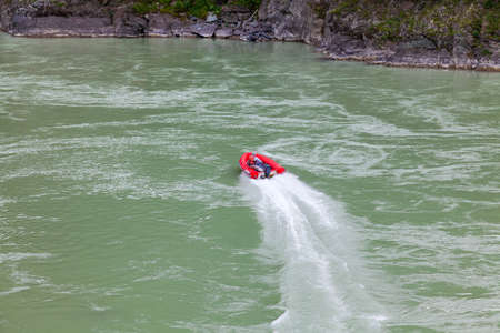 Aerial view of a red rubber motor boat sailing on a green river in the mountains between rocks and cliffの写真素材