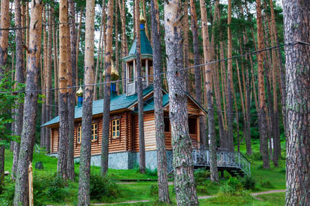 An old antique wooden church or monastery in the forest among a large number of trees with crosses and domes on the roof. Christian Orthodox religion, faith and hermitage.の写真素材
