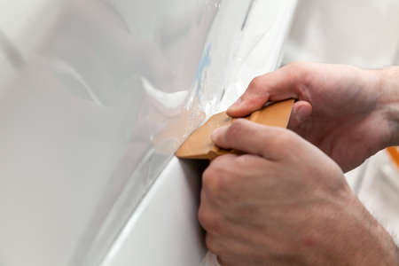 Retrofitting the car with a solid transparent protective film, the master smooths the surface by squeezing air bubbles with a scraper, protecting the vehicles from scratches and chips in the workshopの写真素材
