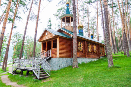 An old antique wooden church or monastery in the forest among a large number of trees with crosses and domes on the roof. Christian Orthodox religion, faith and hermitage.の写真素材