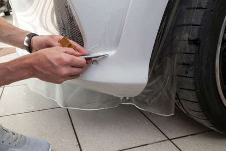 Retrofitting the car with a solid transparent protective film, the master makes an incision with a knife on the coating protecting the vehicles from scratches and chips in the workshop.の写真素材