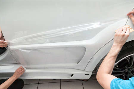 Retrofitting the car with a solid transparent protective film, the master pulls the coating protecting the vehicles from scratches and chips in the workshop.の写真素材