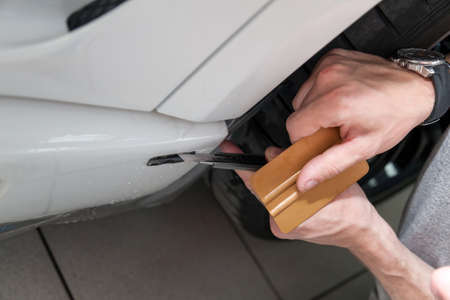 Retrofitting the car with a solid transparent protective film, the master makes an incision with a knife on the coating protecting the vehicles from scratches and chips in the workshop.の写真素材