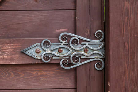 Close-up on a decorative forged hinge in antique style with a twisted pattern on a brown wooden door. Construction and decoration of buildings.の写真素材