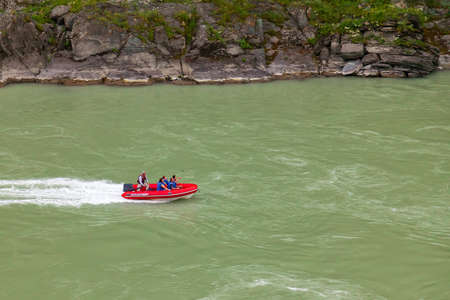 Aerial view of a red rubber motor boat sailing on a green river in the mountains between rocks and cliffの写真素材