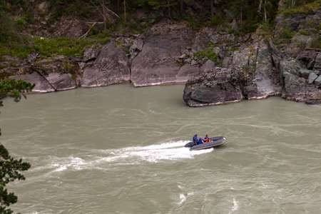 Aerial view of a gray rubber motor boat sailing on a green river in the mountains between rocks and...
