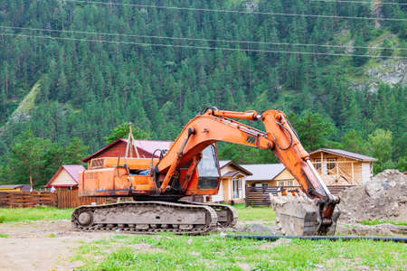 Large orange excavator with a lowered bucket during repair work in the mountains on a summer day.の写真素材