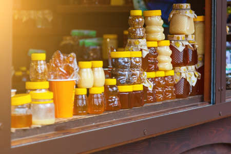 Small jars of golden and white honey in the form of bears stand on a wooden counter in the market during the trade. Health and organic foods with sun shining. Beekeeping and apiaries.の写真素材