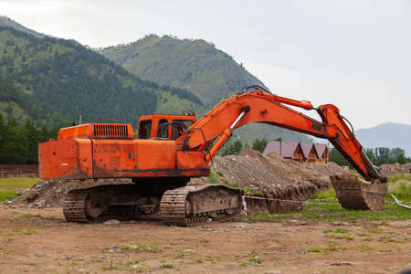 Large orange excavator with a lowered bucket during repair work in the mountains on a summer day.