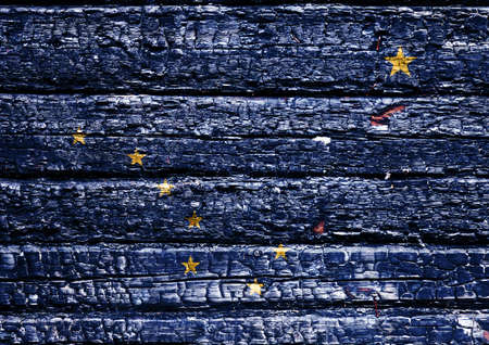 The national flag of the US state Alaska in against a black charred wooden wall on the day of...
