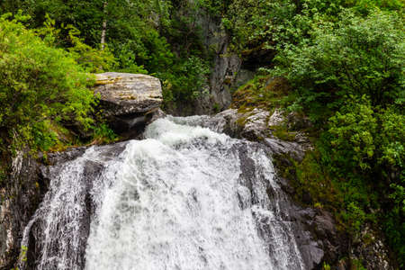 A large waterfall in the back of the Altai Mountains with gray-brown stones near a steep cliff with...