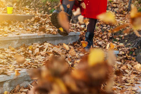 A girl in black boots and a red coat kicks yellow and red foliage strolling in the park alone on a...